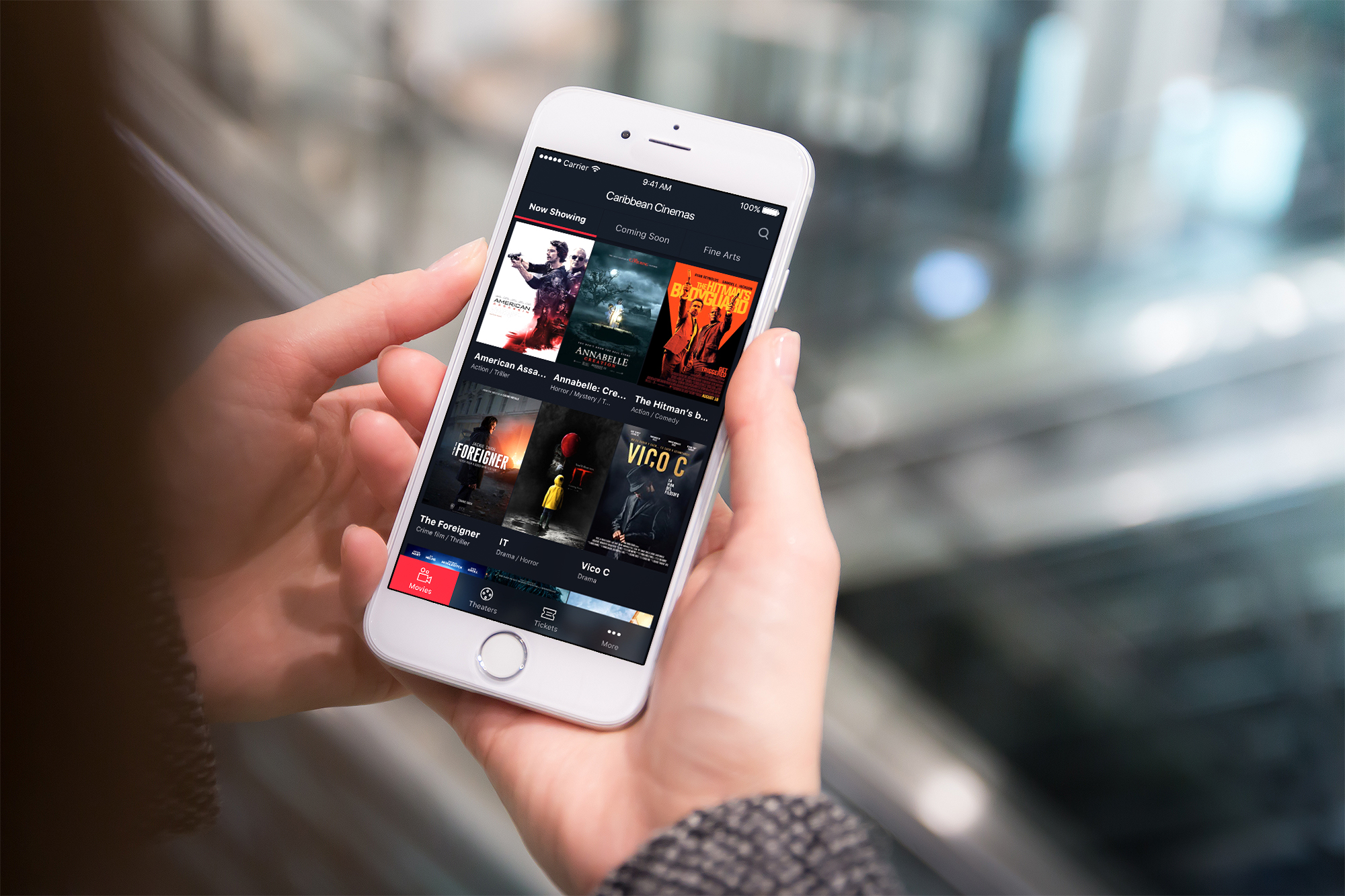 An image of a person holding an iPhone, on the screen, you can see a the of Caribean Cinemas App.